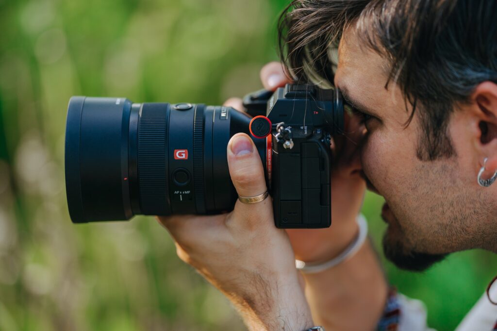 Man photographer taking photos on professional Sony digital camera with G master lens outdoors.