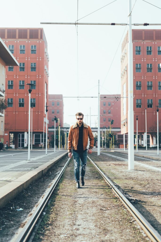 Cool young bearded man walking along city tram lines
