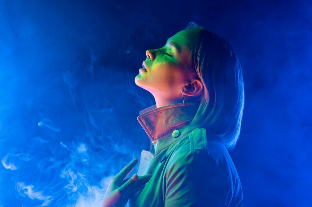 Young woman in neon blue light on smoke,steaming background. Lady in trench coat